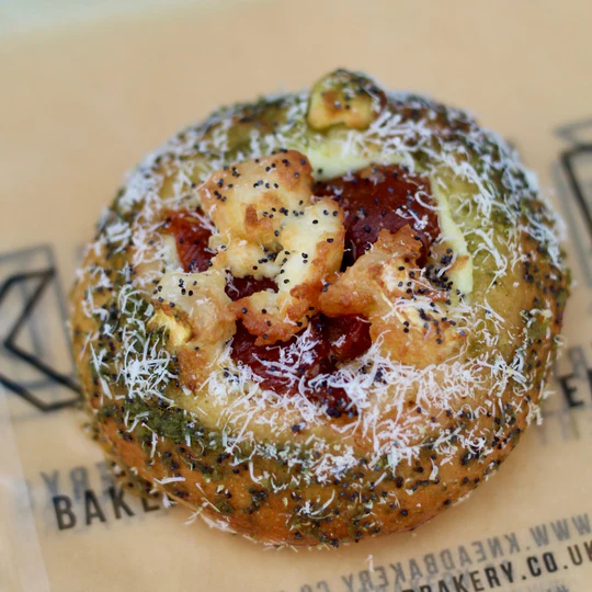 Round savoury pastry with pesto, poppy seeds, and cheese on branded parchment
