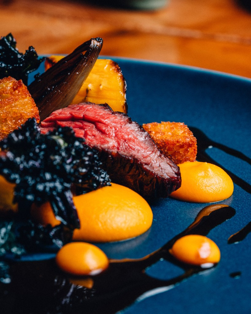 Plated medium-rare steak with orange purée on a dark blue plate
