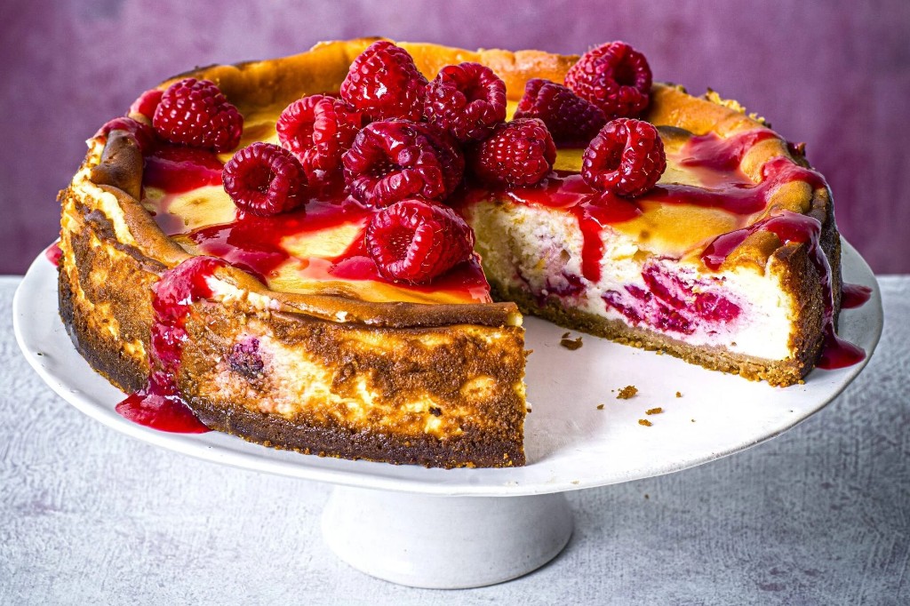 Baked raspberry cheesecake with glossy coulis on a pedestal against a lavender wall